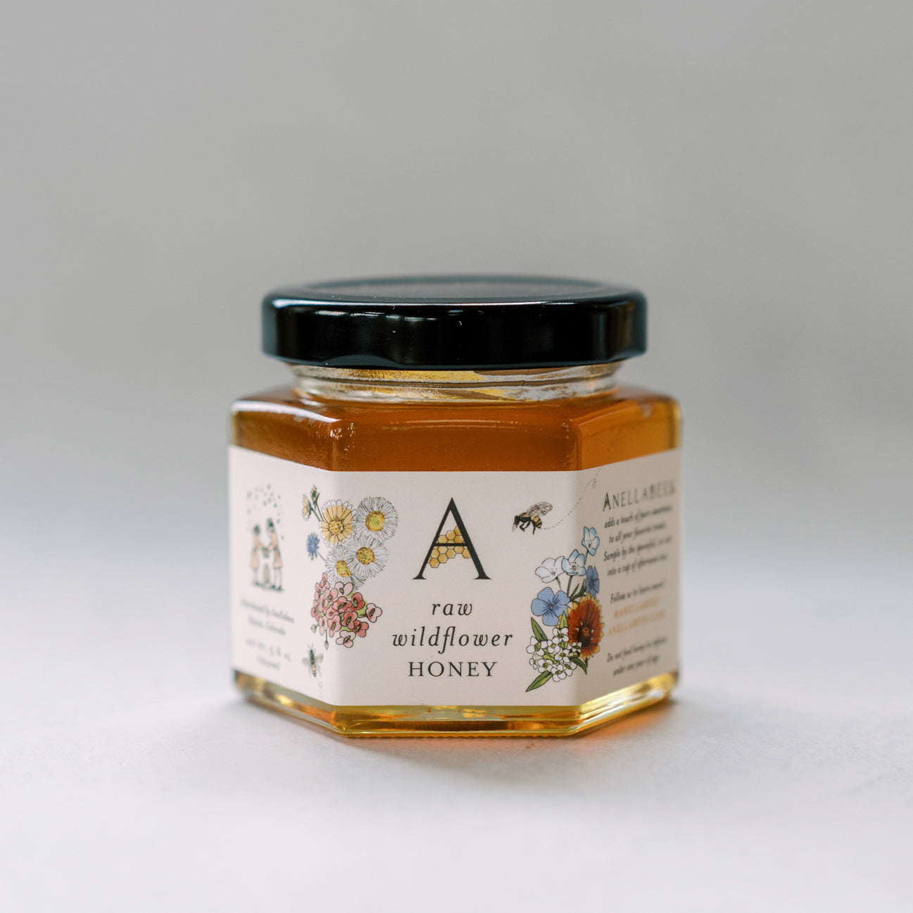 Jar of raw wildflower honey with a decorative label on a light gray background
